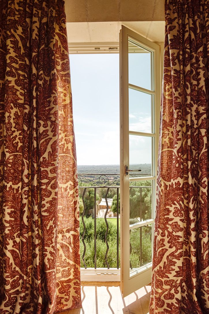 The balcony door open to the gardens, framed by printed linen curtains